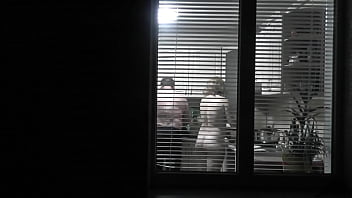 Peeping. Voyeur. Neighbor perv Spycam in evening on street looks out window as nude super-sexy neighbor in kitchen preps dinner for her husband. nude in public. nude at home. Family.  Outdoor